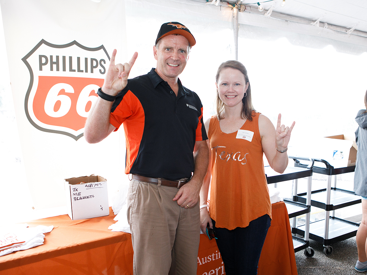 rick neptune and an alumni hold their "horns up" in front of Phillips 66 sign